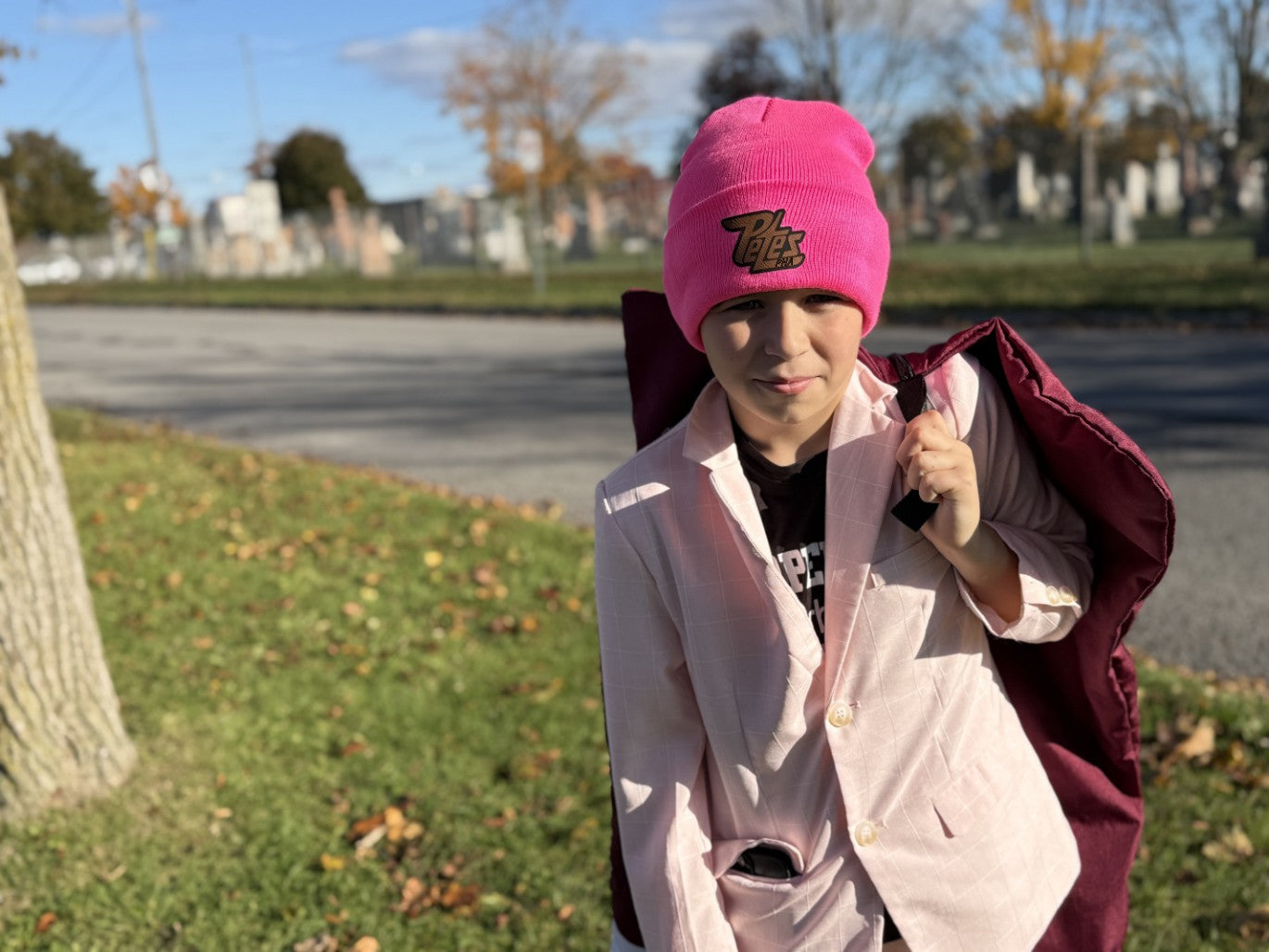 Person wearing a pink beanie and light pink jacket outdoors on a sunny day.